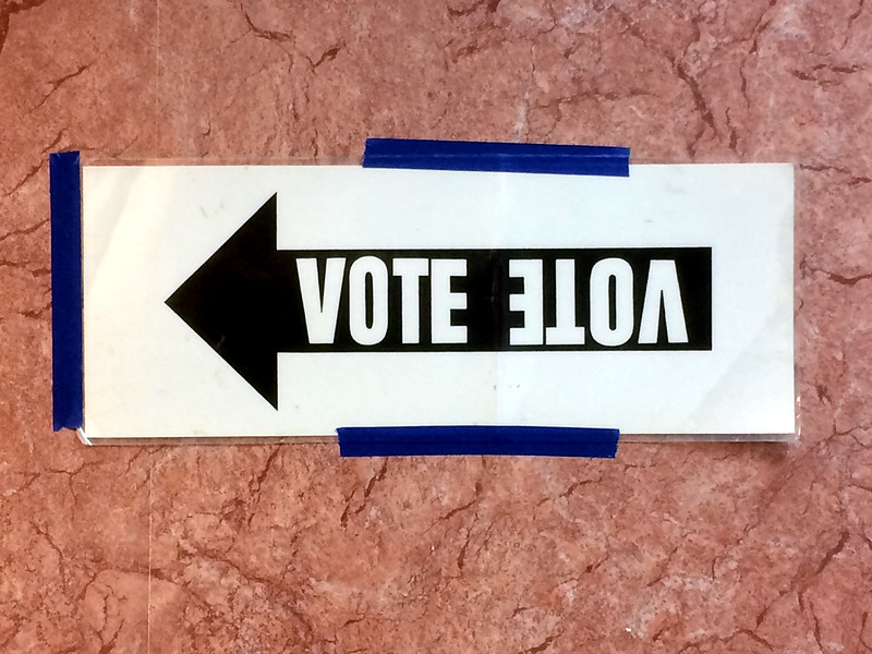 a photo of a sign pasted on a wall that is an arrow with VOTE printed on it, and upside down so it can be used in either direction